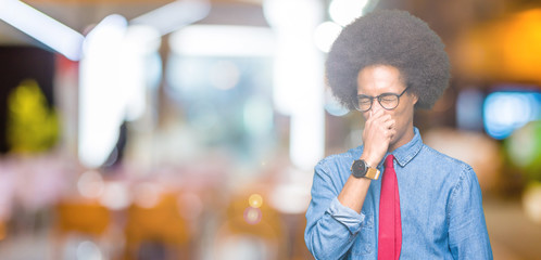Naklejka premium Young african american business man with afro hair wearing glasses and red tie smelling something stinky and disgusting, intolerable smell, holding breath with fingers on nose. Bad smells concept.