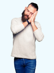 Young blond man wearing casual sweater sleeping tired dreaming and posing with hands together while smiling with closed eyes.