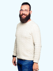 Young hipster man wearing glasses and winter sweater looking away to side with smile on face, natural expression. Laughing confident.
