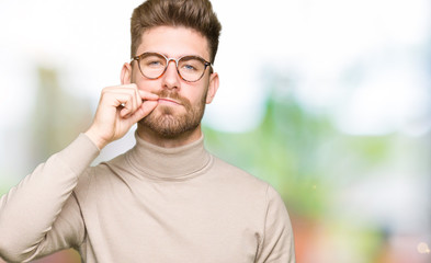 Young handsome business man wearing glasses mouth and lips shut as zip with fingers. Secret and...