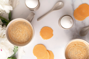 Boiled eggs in ceramic egg cups, two cups of coffee with ceramic spoons on background of beautiful white peony. Breakfast concept. Top view.
