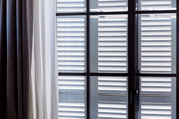 a window with closed shutters and open curtains of white textiles.