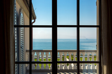 view from the window inside the room on the balcony with balustrades and wooden shutters in the background blue sky with the sea summer sunny morning nobody.