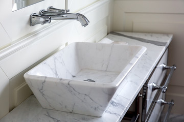 chrome-plated faucet with white marble washbasin and worktop in the bathroom with wood panel walls, close up details.