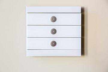 A modern white glass touch sensitive multifunctional light switch with indicators instal on a beige wall close up.