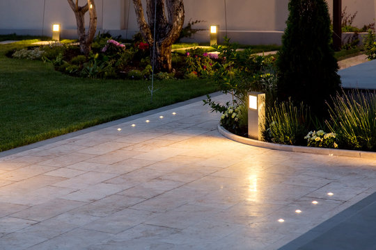 marble tile playground in the backyard of flowerbeds and lawn with ground lantern and lighting in the warm light at dusk in the evening.