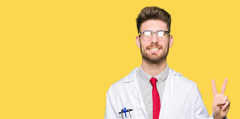 Young handsome scientist man wearing glasses showing and pointing up with fingers number two while smiling confident and happy.