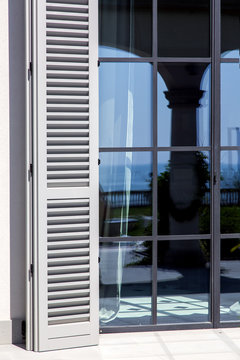 wooden shutters of gray wood are open to sunlight near the panoramic windows with a black frame, close up of the exterior of the house in the Italian style.