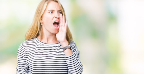 Beautiful young woman wearing stripes sweater over isolated background shouting and screaming loud to side with hand on mouth. Communication concept.