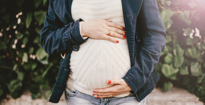 Pregnant Woman In A White Knitted  Sweater Holding Hands On Her Belly. Close Up Stomach