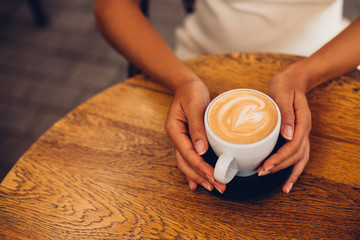 Woman holding cup of coffee cappuccino with heart shaped foam