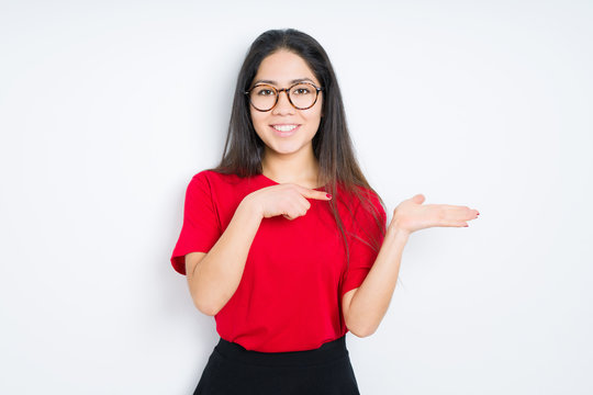 Beautiful brunette woman wearing glasses over isolated background amazed and smiling to the camera while presenting with hand and pointing with finger.
