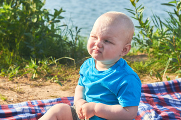 Portrait of a funny boy who grimaces, on the river bank on a summer day