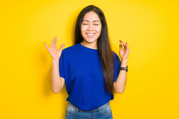Beautiful brunette woman wearing blue t-shirt over yellow isolated background celebrating mad and...