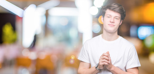 Young handsome man wearing casual white t-shirt over isolated background Hands together and fingers crossed smiling relaxed and cheerful. Success and optimistic