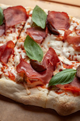 Macro close up of roman square pizza on a thick dough with mozzarella, pastrami, sweet plum and basil leaves, served on a wooden table