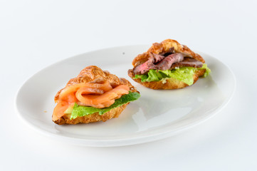 Freshly baked french croissants with cream cheese, green leaves and smoked salmon and smoked pork with greens, isolated on white