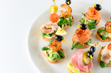 Variety of cold appetizers for party buffet or banquet ? different states canapes on skewers with greens, meat, cheese and seafood isolated on white