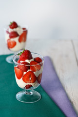 Whipped cream and strawberries served in a glass. Purple and dark green napkins, white wooden table, high resolution