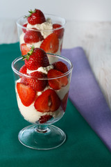 Whipped cream and strawberries served in a glass. Purple and dark green napkins, white wooden table, high resolution