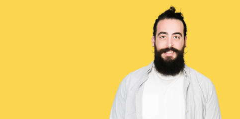 Obraz premium Young man with long hair, beard and earrings with a happy and cool smile on face. Lucky person.