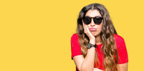 Young beautiful woman wearing red t-shirt and sunglasses thinking looking tired and bored with depression problems with crossed arms.
