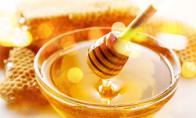 Honey with spoon in glass bowl on glossy background