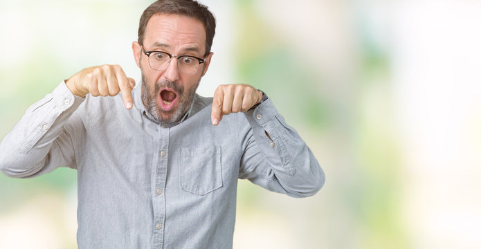 Handsome middle age elegant senior man wearing glasses over isolated background Pointing down with fingers showing advertisement, surprised face and open mouth