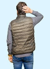 Middle age handsome man wearing winter vest Backwards thinking about doubt with hand on head