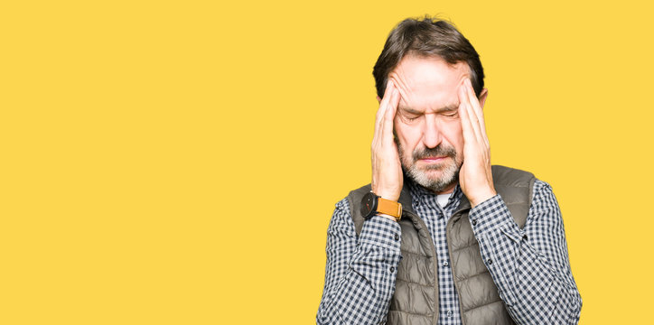 Middle age handsome man wearing winter vest with hand on head for pain in head because stress. Suffering migraine.