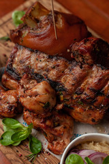Close up of various hot meat snacks for beer served on wooden dish board: big pork knuckle, BBQ pork ribs, chicken thigh kebab with mustard and sauced