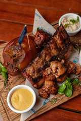 Close up of various hot meat snacks for beer served on wooden dish board: big pork knuckle, BBQ pork ribs, chicken thigh kebab with mustard and sauced