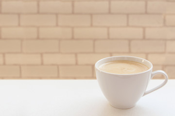white wide cup of coffee, cappuccino with milk, cocoa on a white table against the background of a light brick wall, side view, save space