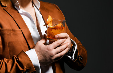 Young business man in white shirt and stylish jacket holds a rocks glass with beverage