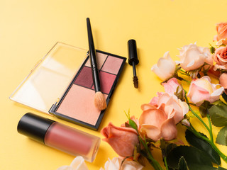 Obraz na płótnie Canvas Lipstick, palette, mascara and brush on yellow theme make up on roses frame for promotion. Set of decorative cosmetics. Copy space. Ideal for beauty blog. Flat lay for beauty service