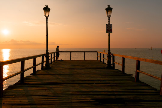 Wooden dock, sea and fisherman in the sunrise. Beautiful summer scenery © stivog