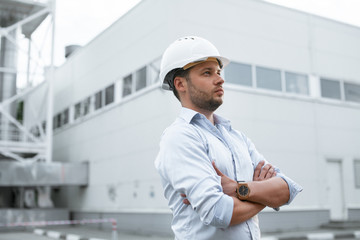 Young handsome male engineer in hardhat standing on the background of water or gas pipes. Concept of boiler station. Pipeline accessories closeup. Heating station manager doing his job outdoor. .
