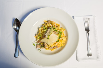 Tagliatelle pasta with cheese and chicken meat served on a white plate