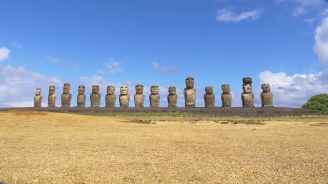 AERIAL: Mysterious monoliths with human faces in Chile all facing the same direction. Breathtaking shot of a row of famous moai statues under the clear blue summer sky on a remote volcanic island.