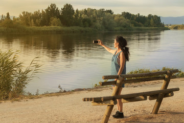 Fototapeta na wymiar Brunette young woman photographing a landscape with river