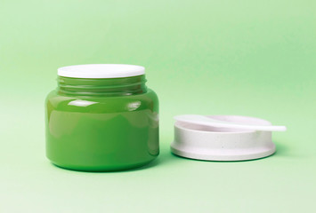Green jar with white cream and plastic spatula on background, side view, copy space