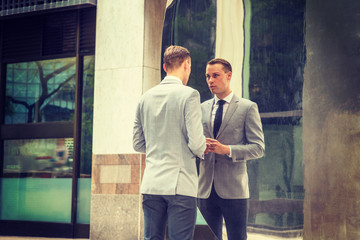 Young Businessman Fashion in New York City. Young Man wearing gray blazer, white shirt, black tie, black pants, standing on street in front of metal mirror, looking at reflections, thinking..