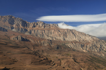 Obraz premium Majestic mountain view - rocky peaks with brownish withered grassy slopes under blue sky with blindingly white clouds