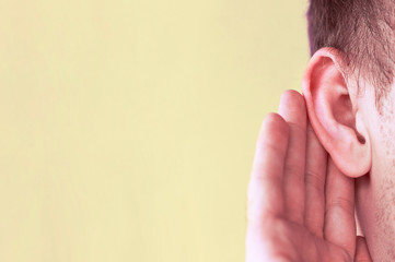 Man listens attentively with her palm to her ear, close up, news concept
