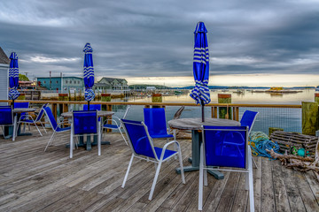 Picnic Tables with Umbrellas Set on a Dock Overlooking a New England Harbor on a Cloudy Day