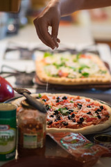Hand sprinkling cheese onto pizza with ingredients surrounding it