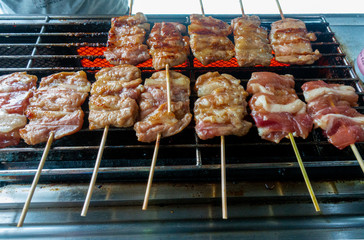 Thai grilled pork, some still raw, cooking on a small barbecue grill machine.