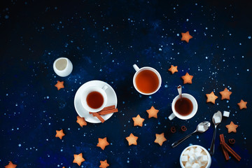 Teatime with star-shaped cookies. White porcelain cups on a starry sky background. Astronomy and constellation flat lay with copy space
