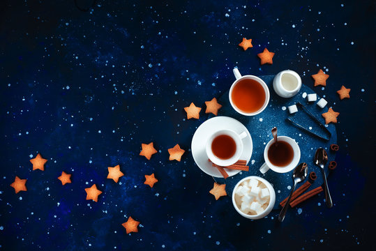 Teatime with star-shaped cookies. White porcelain cups on a starry sky background. Astronomy and constellation flat lay with copy space