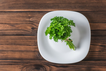 Bunch of parsley on a white plate on a wooden table. Flat lay.